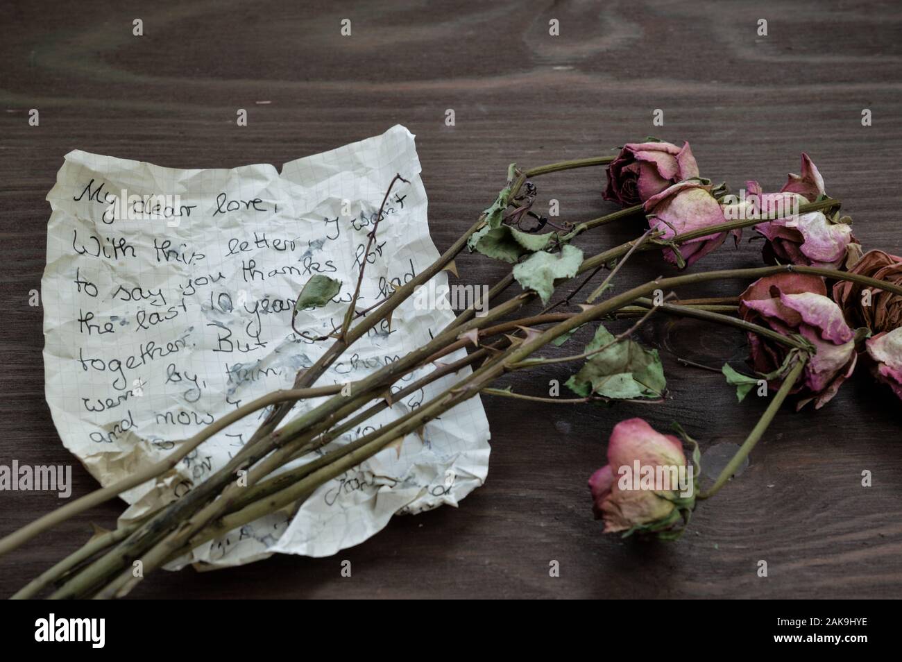 old rumpled farewell letter with withered roses on brown wooden table as keepsake for a long lost love Stock Photo