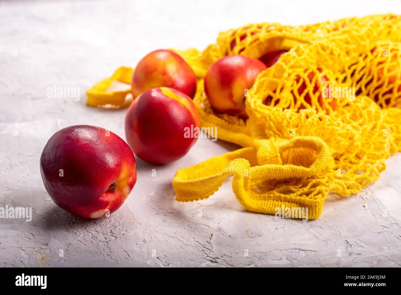 Nectarines in yellow string mesh reusable bag on the table Stock Photo