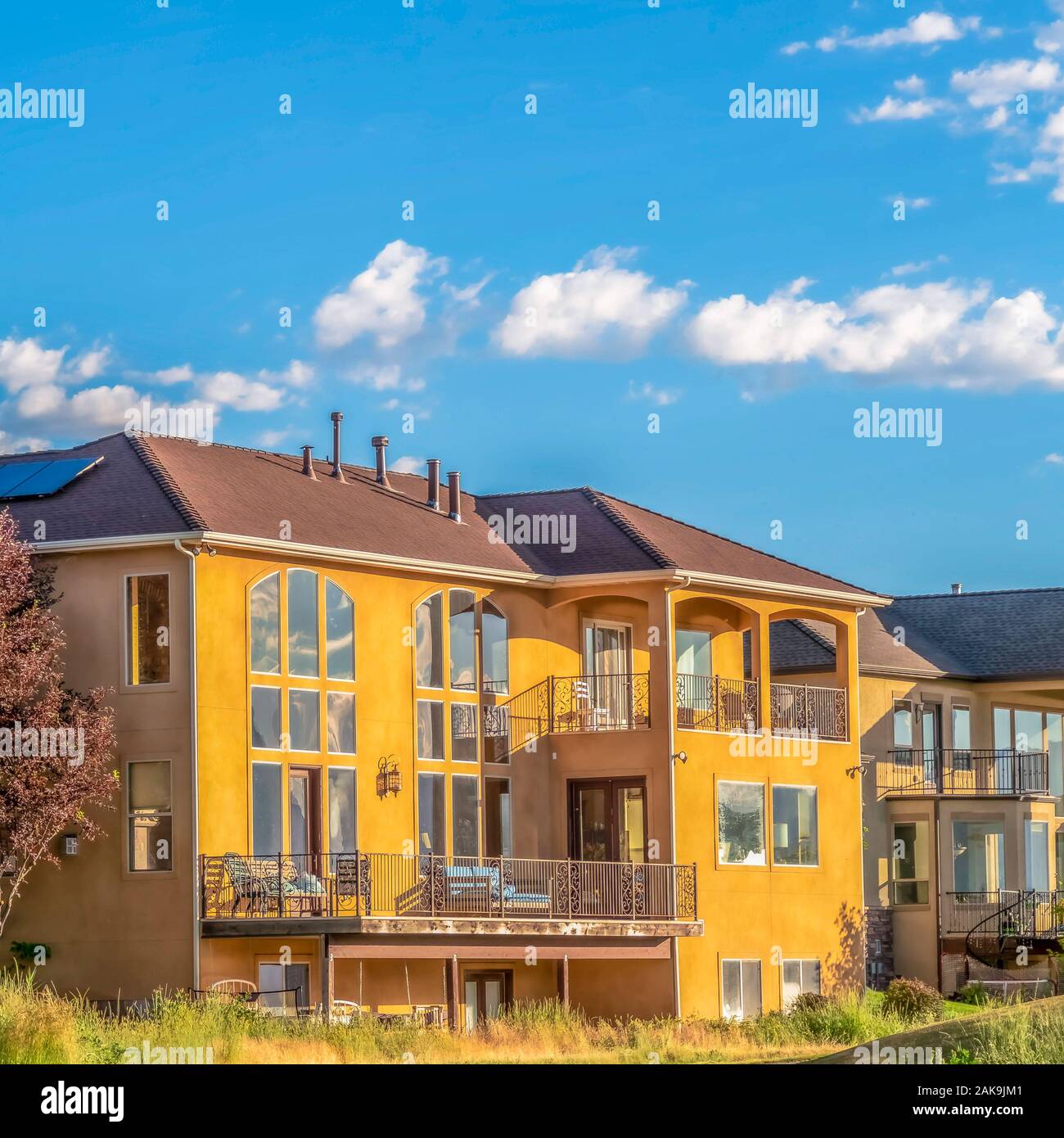 Square frame Road amidst grassy land in front of beautiful homes against blue sky with clouds Stock Photo