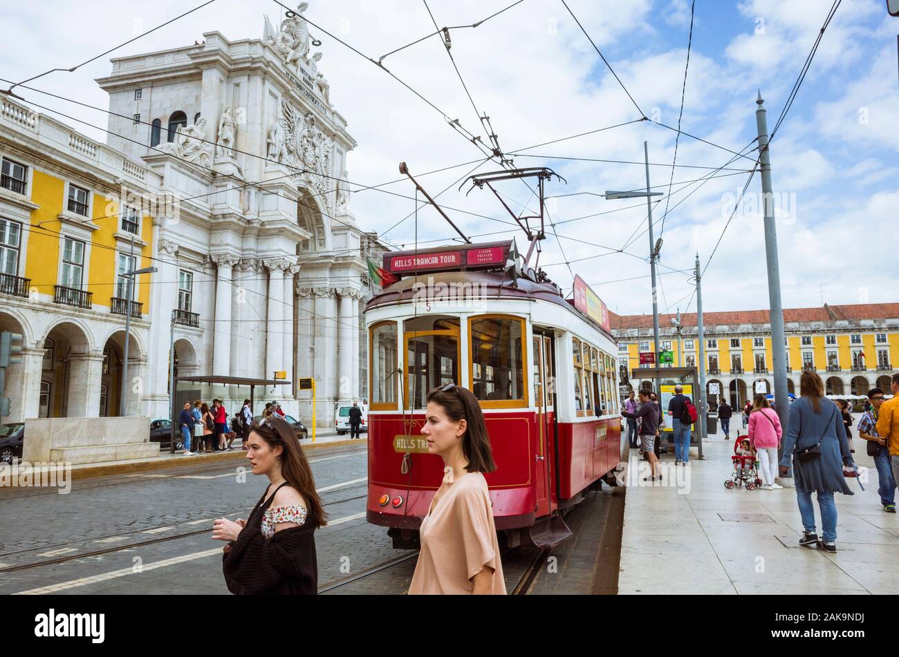 Lisbon, Portugal : Two young women walk past an old red tram next to the Rua Augusta Triumphal  Arch at Praça do Comércio square. Stock Photo