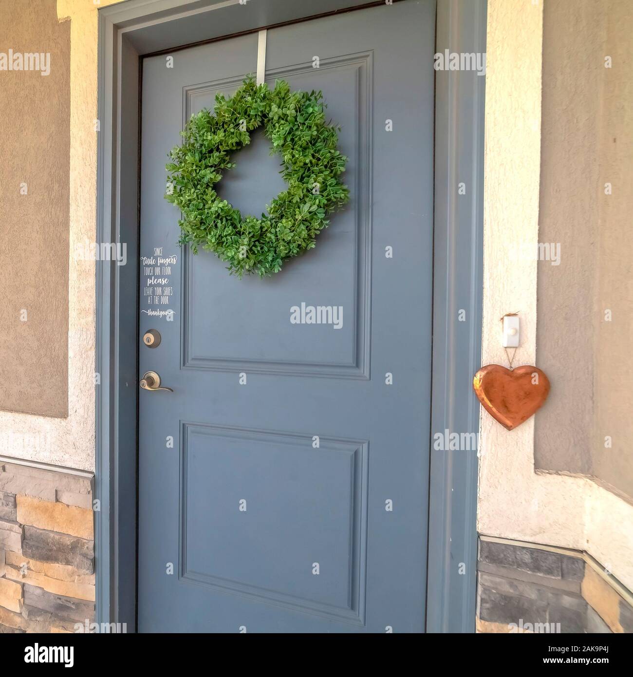 Square Home exetrior with close up on blue gray front door decorated with green wreath Stock Photo