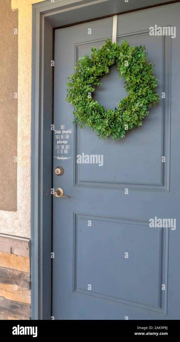 Vertical frame Home exetrior with close up on blue gray front door decorated with green wreath Stock Photo