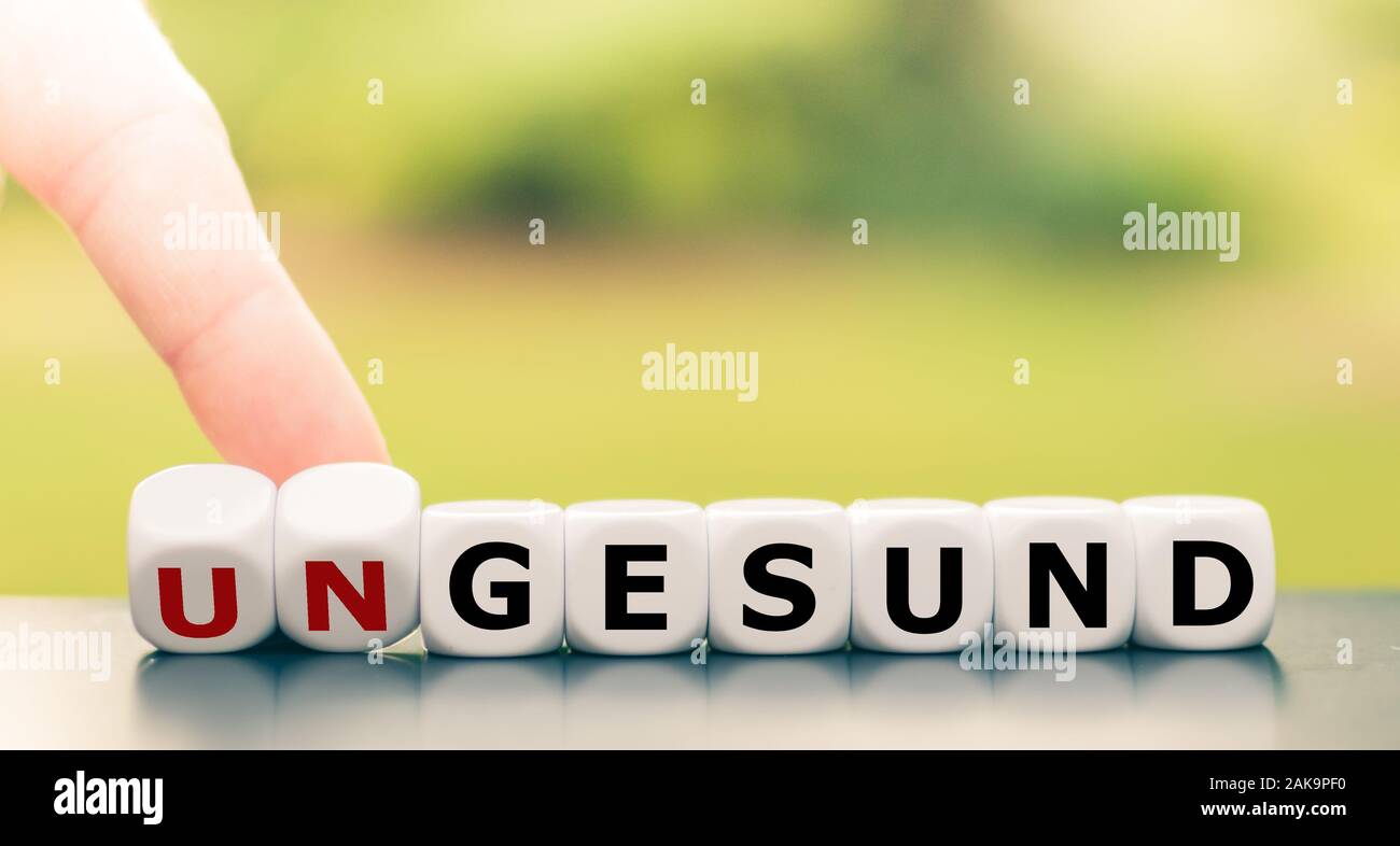Hand turns dice and changes the German word 'ungesund' ('unhealthy' in English) to 'gesund' (' healthy' in English). Stock Photo