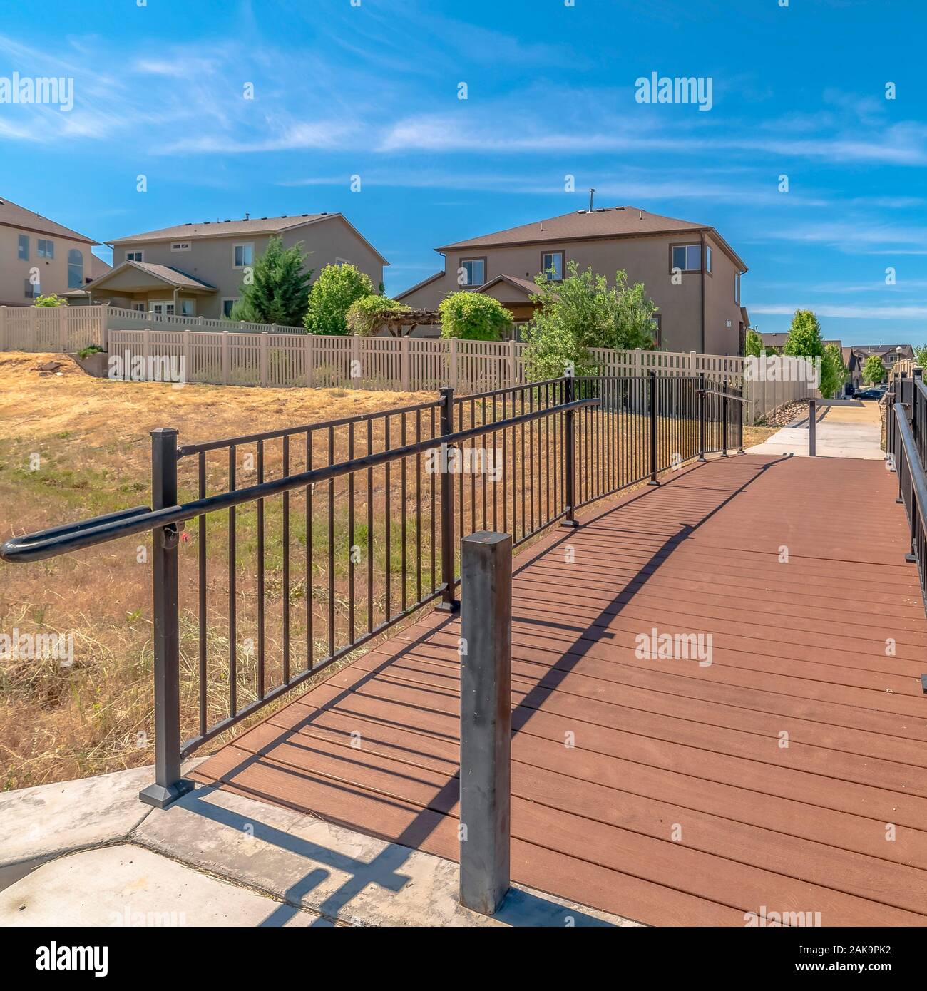 Square Bridge over grassy terrain leading to houses with sunny blue sky ...
