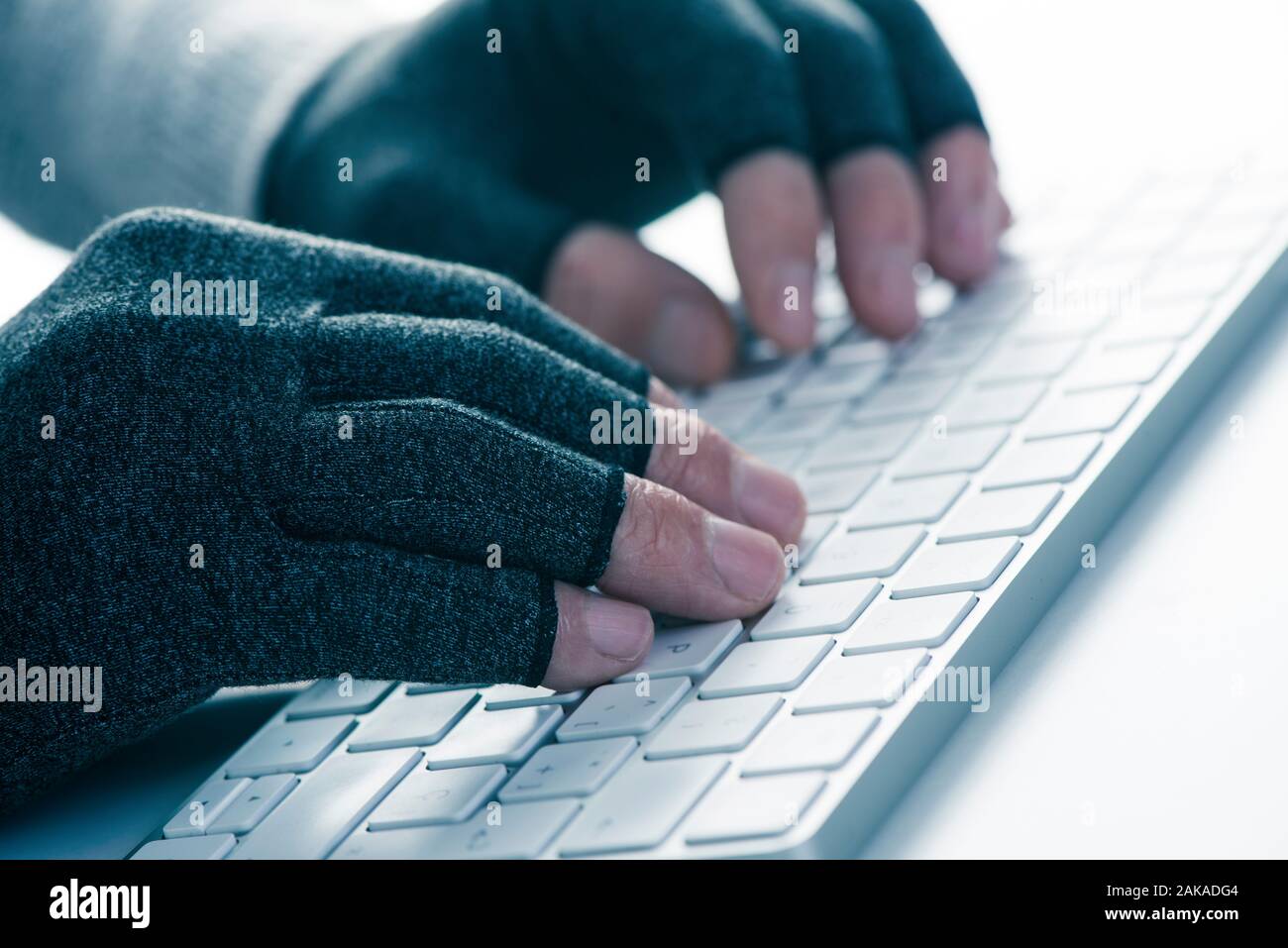 closeup of a caucasian man wearing a pair of compression gloves while is typing on a computer keyboard Stock Photo