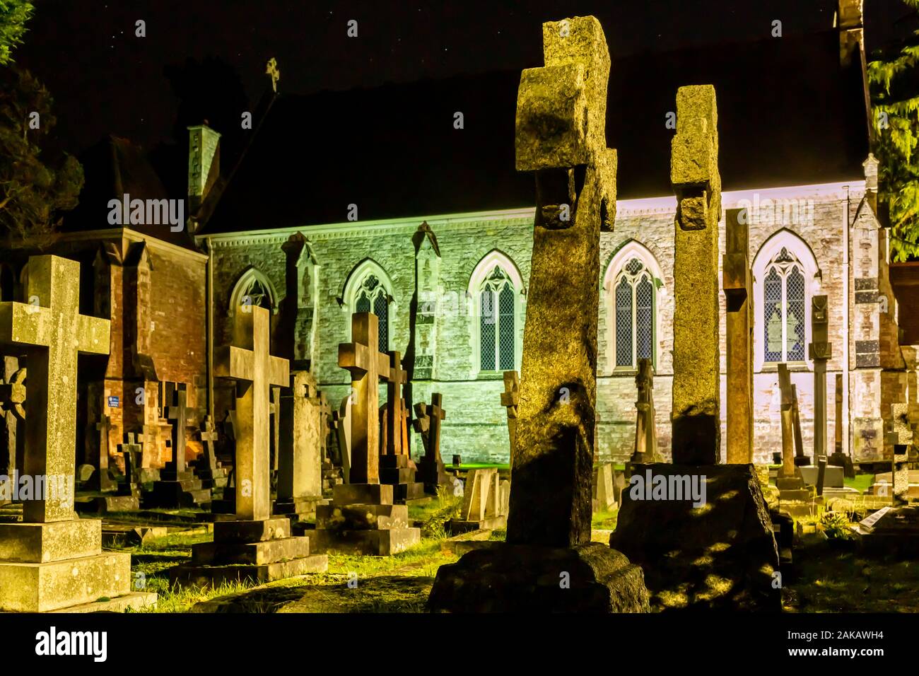 Colour night-time photograph within grave yard with grave stones illuminated by street-light. Stock Photo
