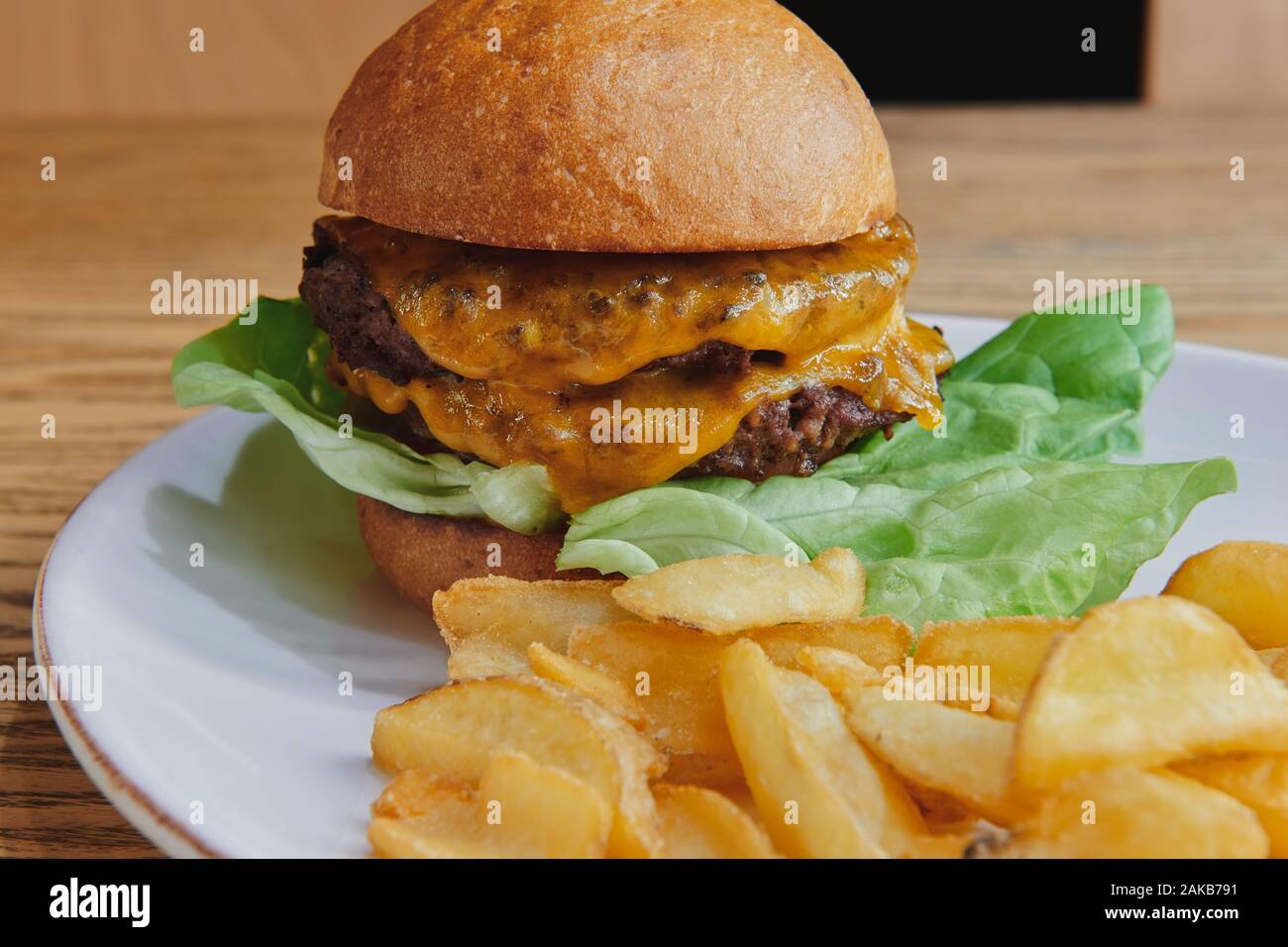 Double beef burger with double cheese and salad. Served with potato dippers on the white plate. American cuisine closeup. Stock Photo