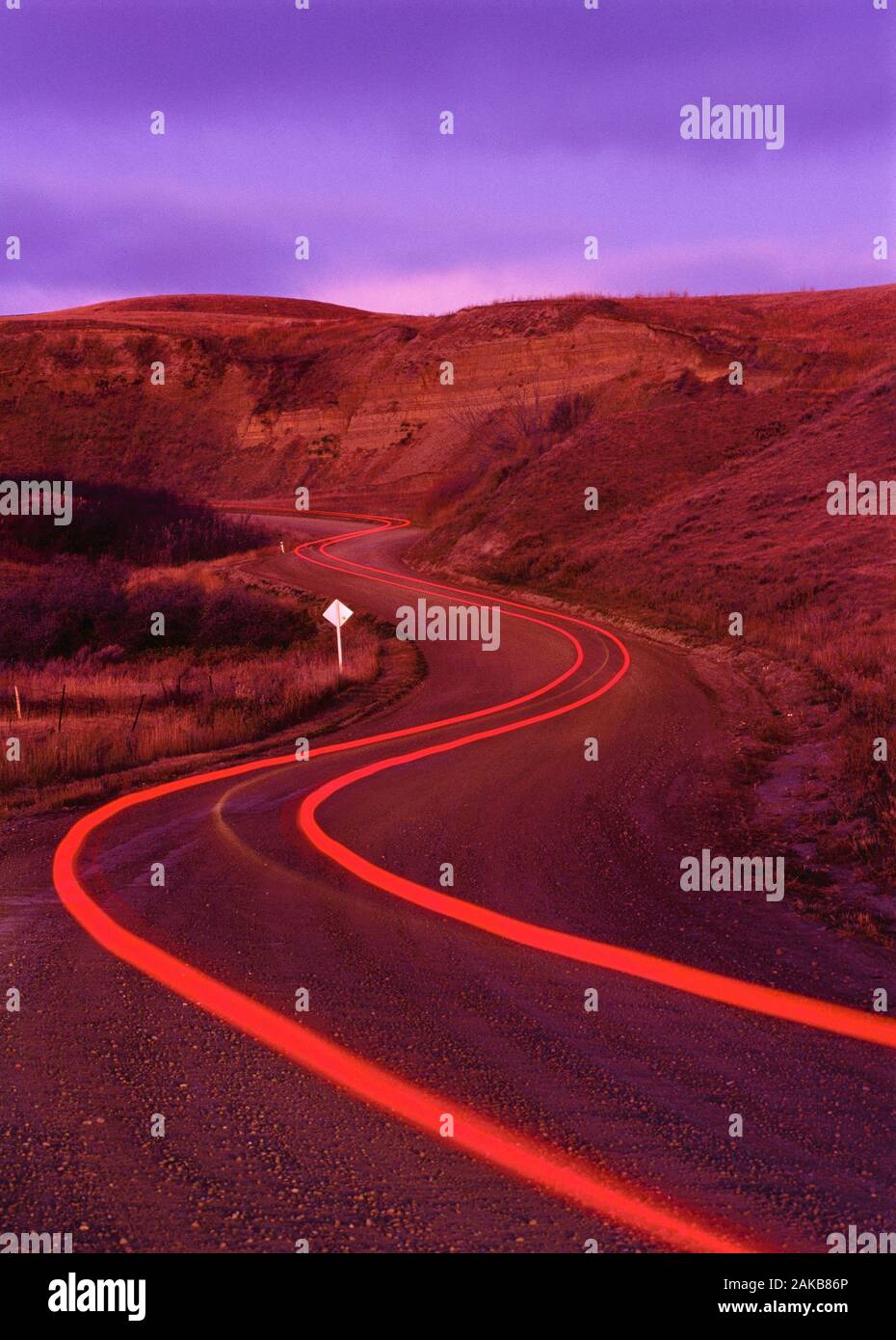 Light trails on winding road at sunset, Drumheller, Alberta, Canada Stock Photo