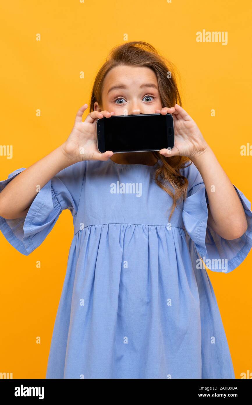 vertical portrait of a girl with a phone in a horizontal position with a layout on a yellow background Stock Photo