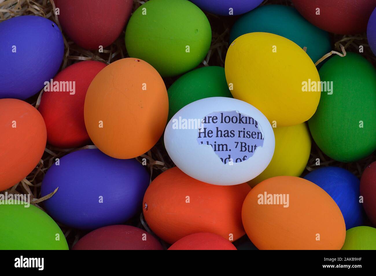 bright white egg with broken shell and the bible passage HE HAS RISEN inside between many multicolored Easter eggs Stock Photo