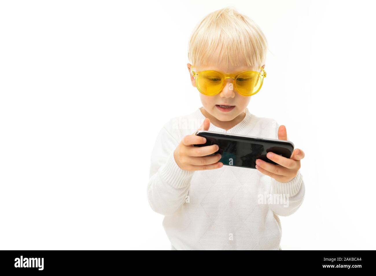 Caucasian blond child plays a game on the phone in a horizontal position on a white background Stock Photo