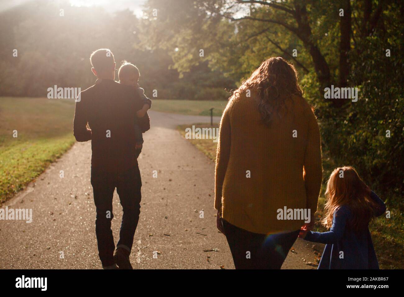 A family walks together holding hands in a park in the setting sun Stock Photo