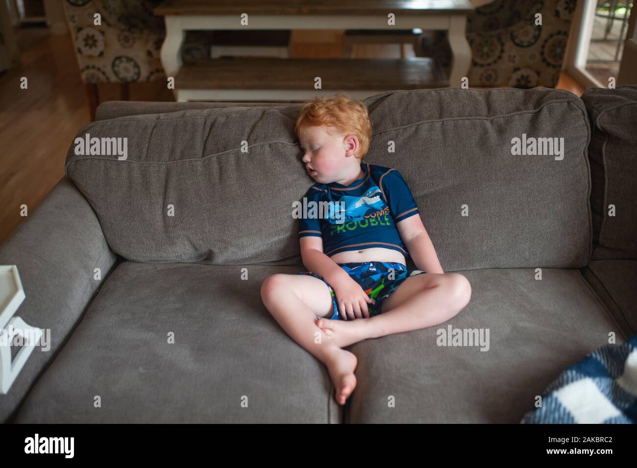 exhausted toddler boy 2-3 years old asleep sitting up on couch at home Stock Photo