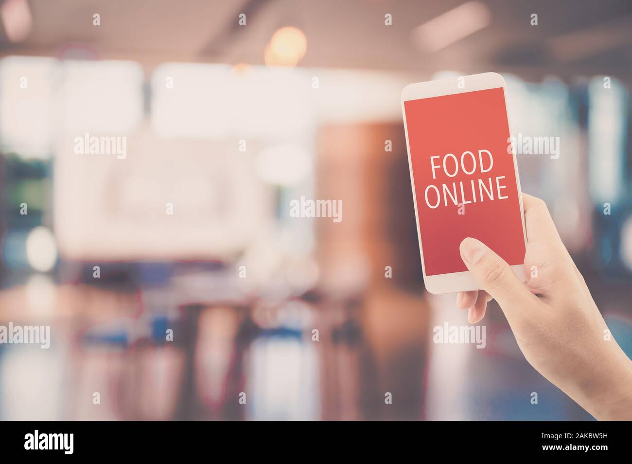 Tay cầm điện thoại đặt món ăn trực tuyến trên nền nhà hàng mờ giúp bạn tiết kiệm thời gian và công sức. Bạn chỉ cần ngồi lại, lướt qua danh sách thực đơn và chọn lựa những món ăn yêu thích của mình.