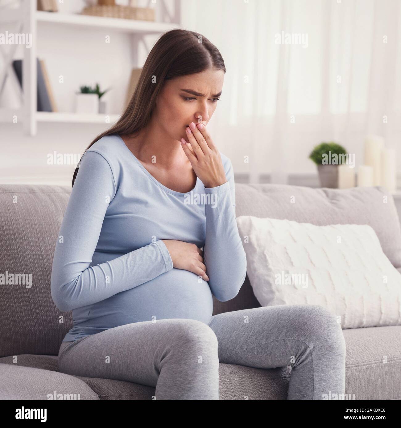 Pregnant Woman Feeling Sick Having Pregnancy Morning Sickness Sitting On Couch At Home Stock Photo