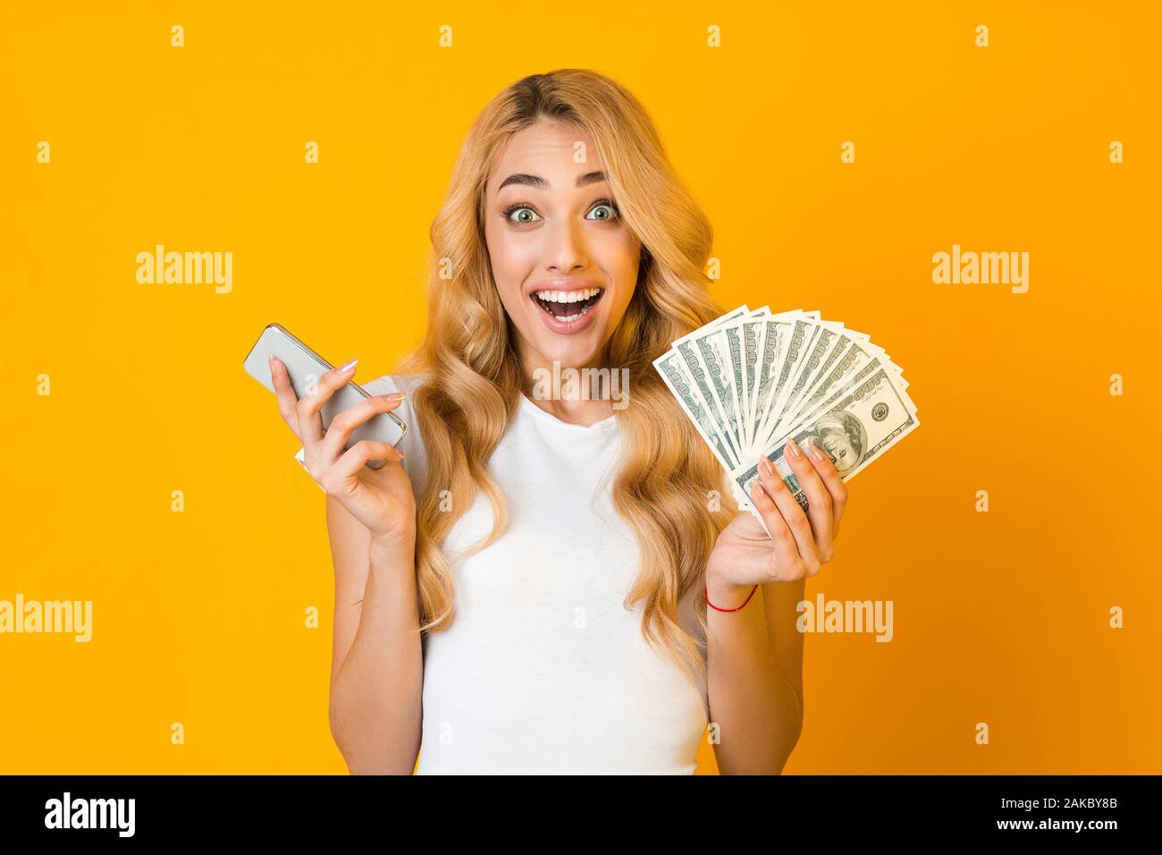 Make money online. Excited woman holding smartphone and bunch of money over  yellow background Stock Photo - Alamy