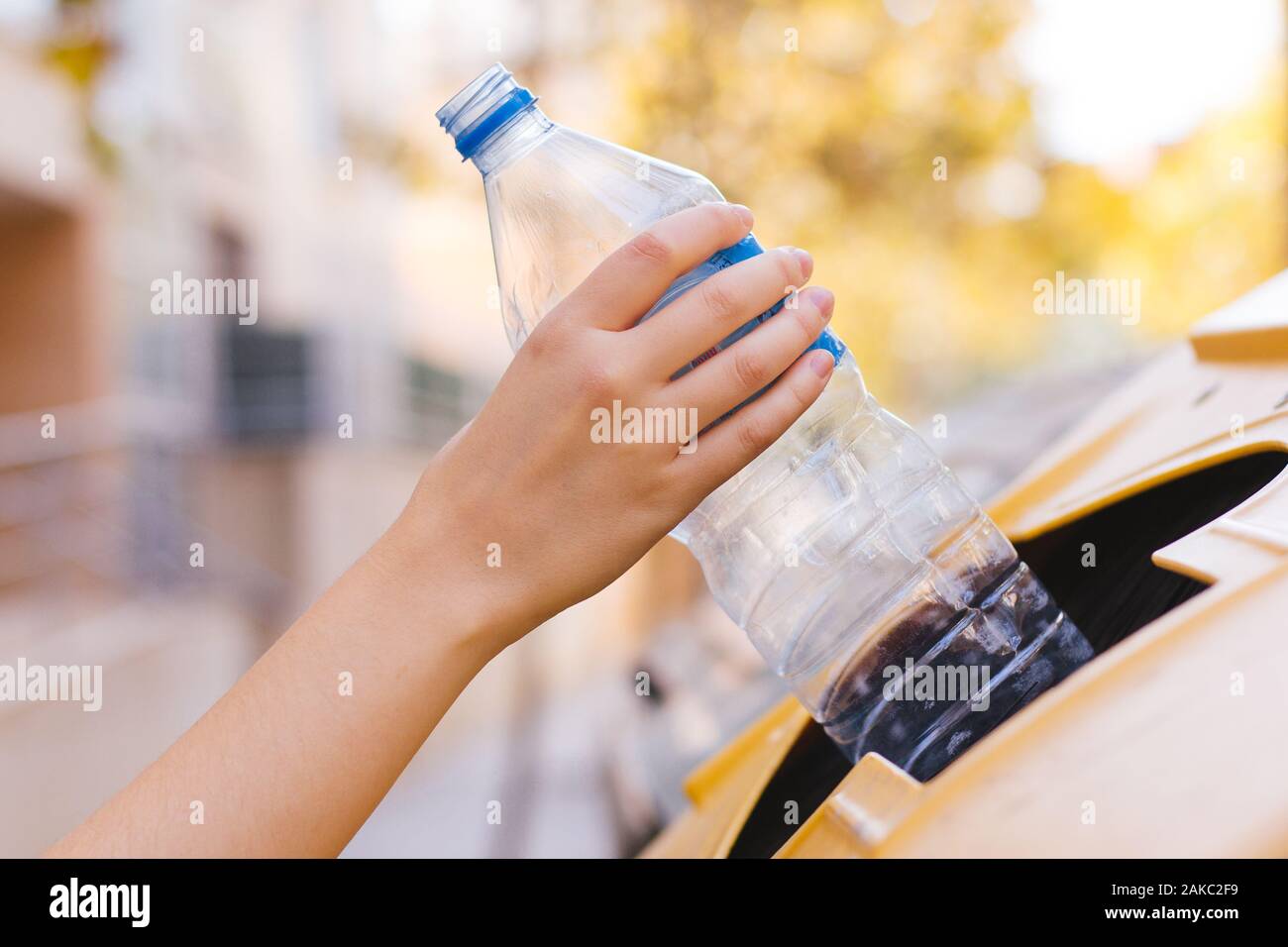 Stock photo of a woman's hand recycling a plastic bottle in a yellow container to save the environment Stock Photo