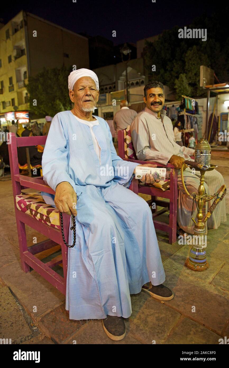 Egypt, Upper Egypt, Aswan, old trader of the turbaned souk, a rosary in his hand, banknotes in the other, sitting near a hookah Stock Photo