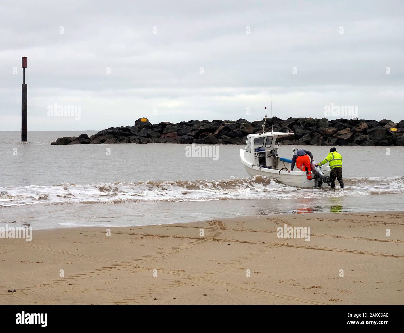 Longshore fishermen launch a small fibreglass boat from the beach at Sea Palling, Norfolk in the shelter of a rock island sea defence structure. Stock Photo