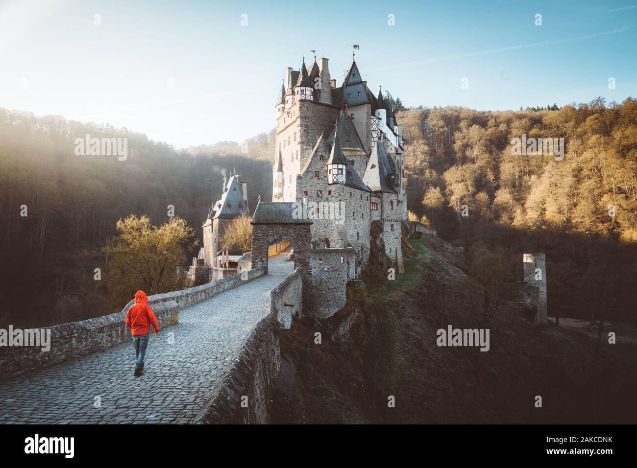 Panorama view of young explorer with backpack taking in the view at famous Eltz Castle at sunrise in fall, Rheinland-Pfalz, Germany Stock Photo