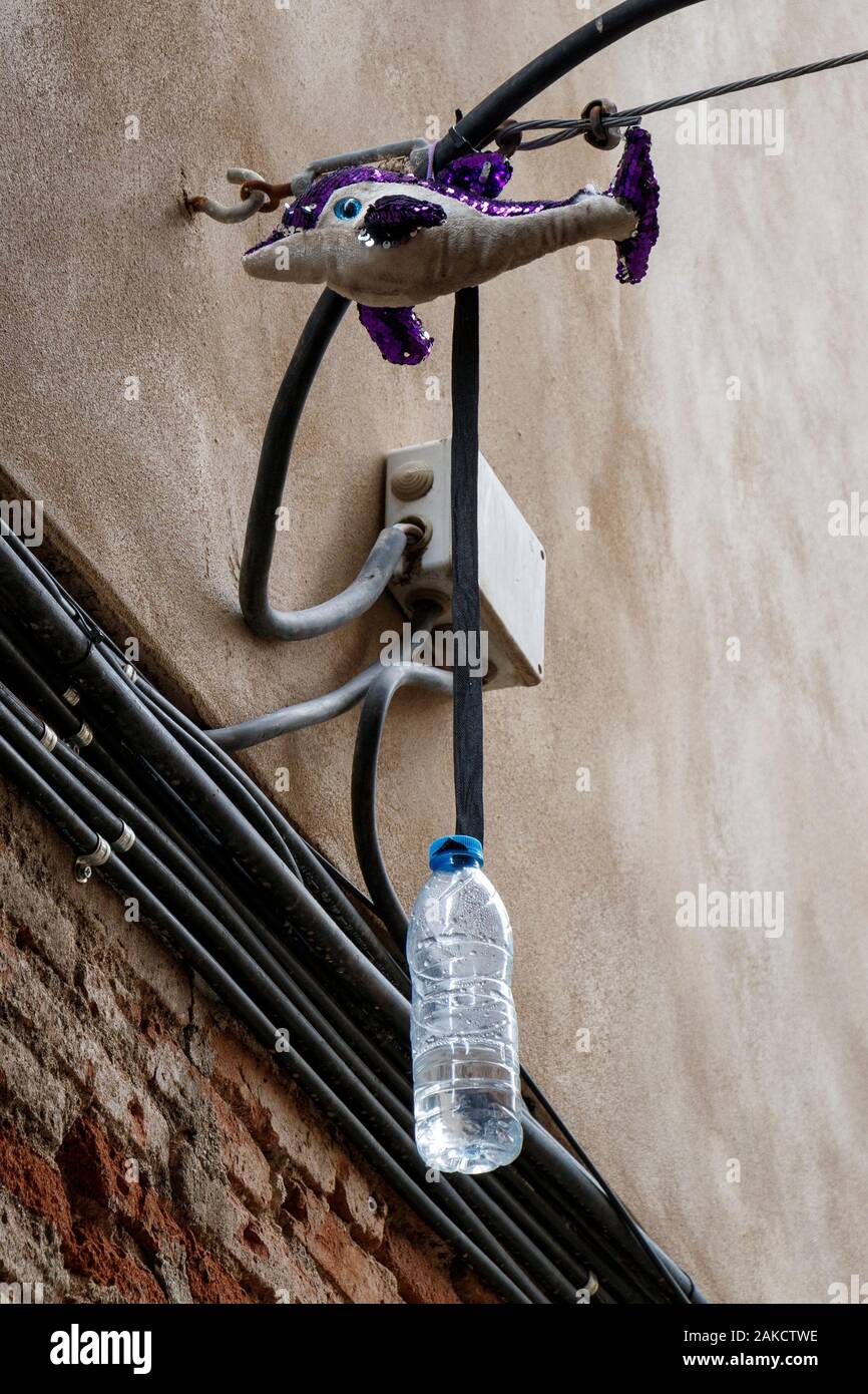 Obscure wall bracket holding a stuffed toy dolphin and a hanging plastic water bottle, Barcelona, Spain. Stock Photo