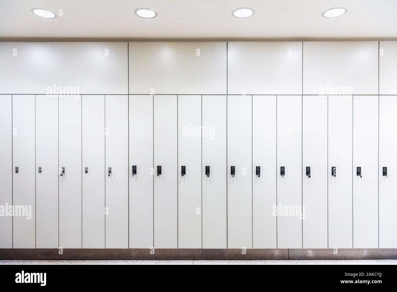 Luxury lookers in a row, in artificial light. White metal wardrobes. Cloakroom with white lockers. Back to school context. Dressing room interior. Stock Photo