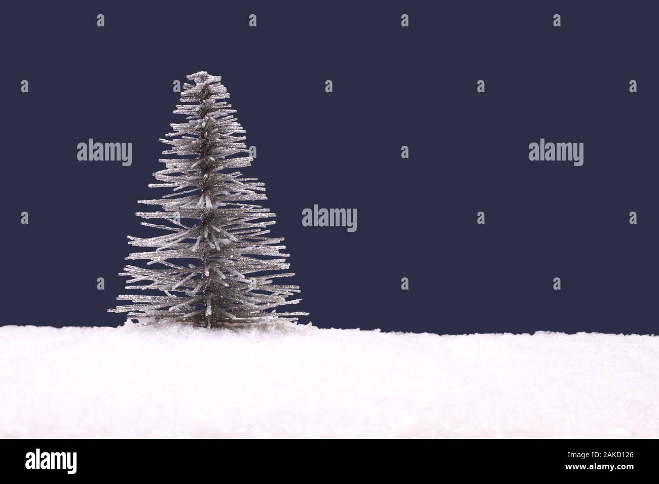 Toy silver Christmas tree on artificial white snow against navy blue background Stock Photo