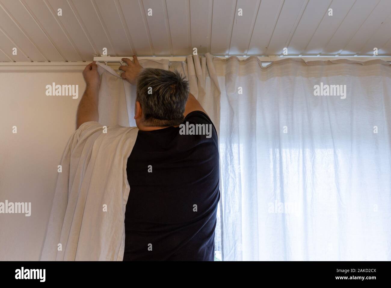 Hands of man installing curtains over window Stock Photo