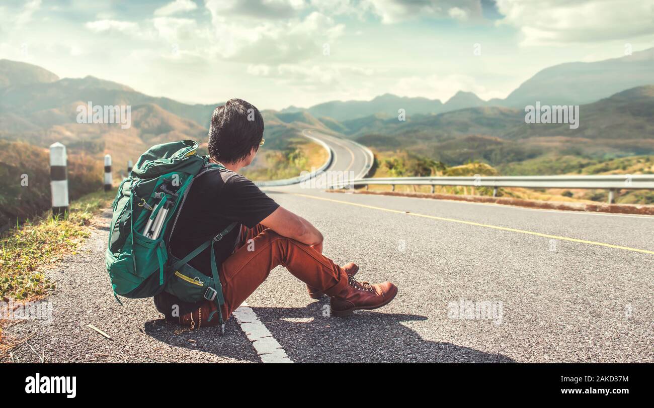 Young man sitting on the roadside. Backpackers, Travel and Holiday concepts. Stock Photo