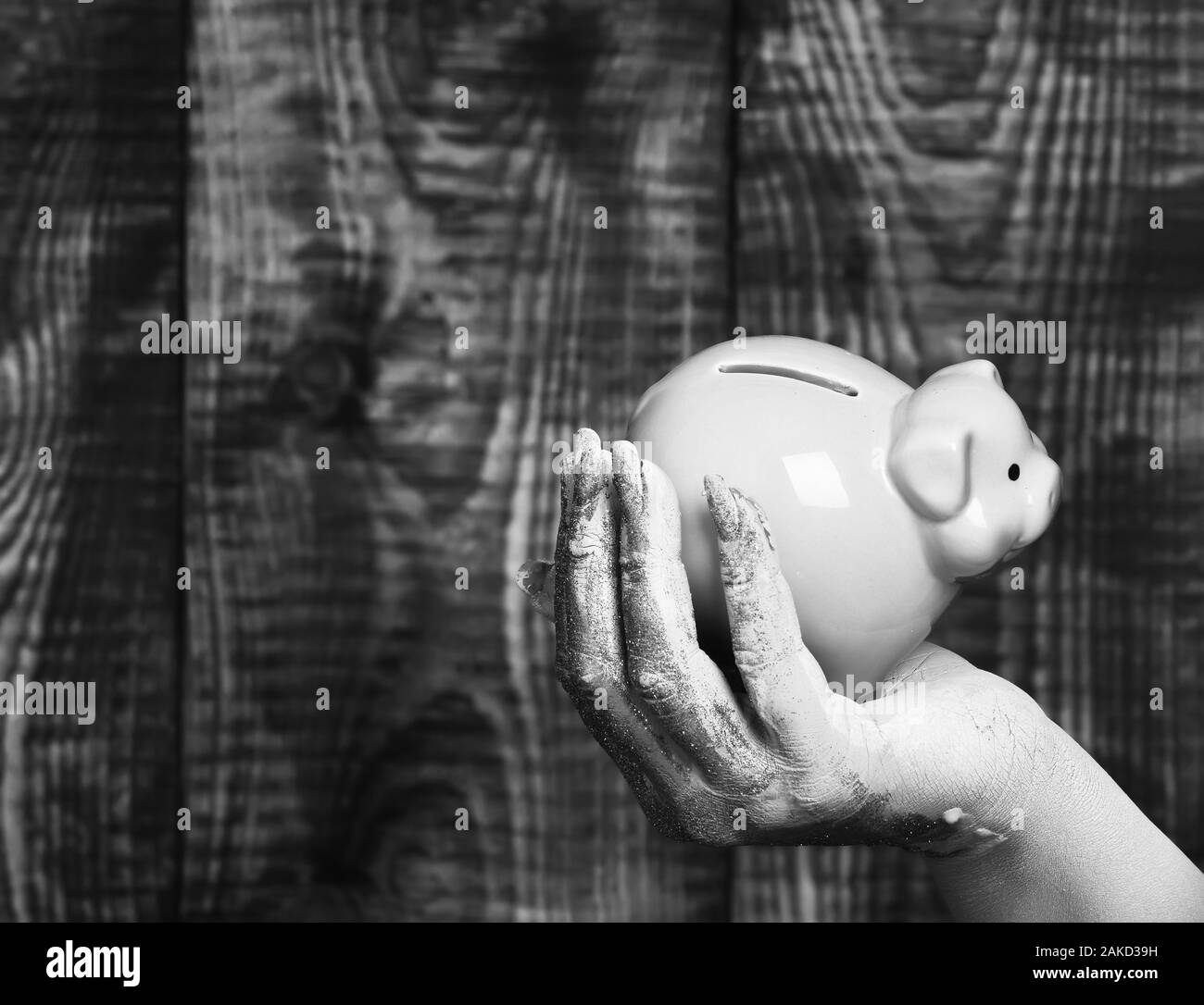 female hand smeared in golden paint or glister holding selective focus pink piggy pig bank on brown vintage studio background, copy space Stock Photo