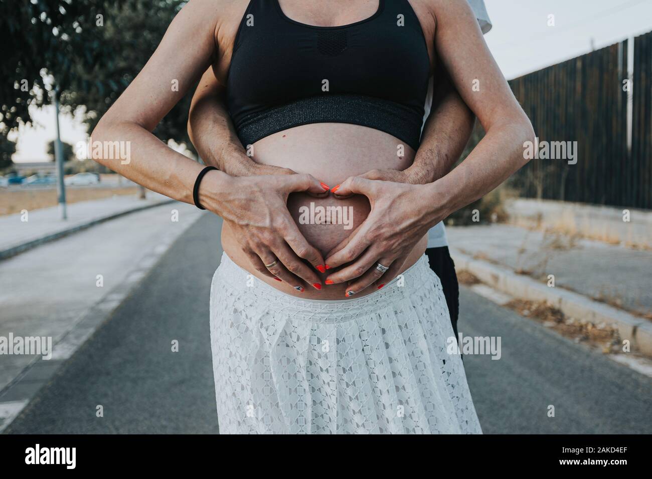 Pregnant belly with fingers heart symbol. Beautiful young pregnant woman and her husband together caressing her pregnant belly Stock Photo