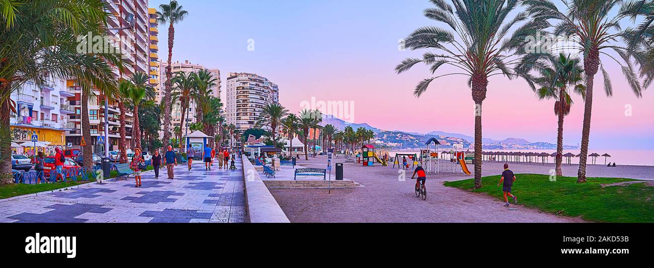 MALAGA, SPAIN - SEPTEMBER 26, 2019: The evening walk in Paseo Maritimo promenade along the scenic Malagueta beach with lush palm trees and purple sky, Stock Photo