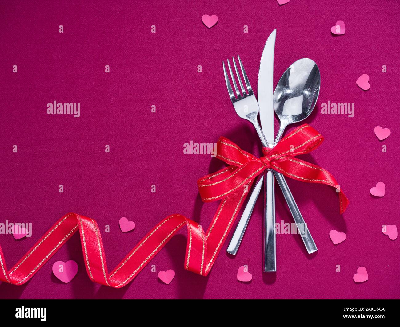 Fork, knife and spoon tied with red ribbon on pink cloth. Celebration food concept Stock Photo