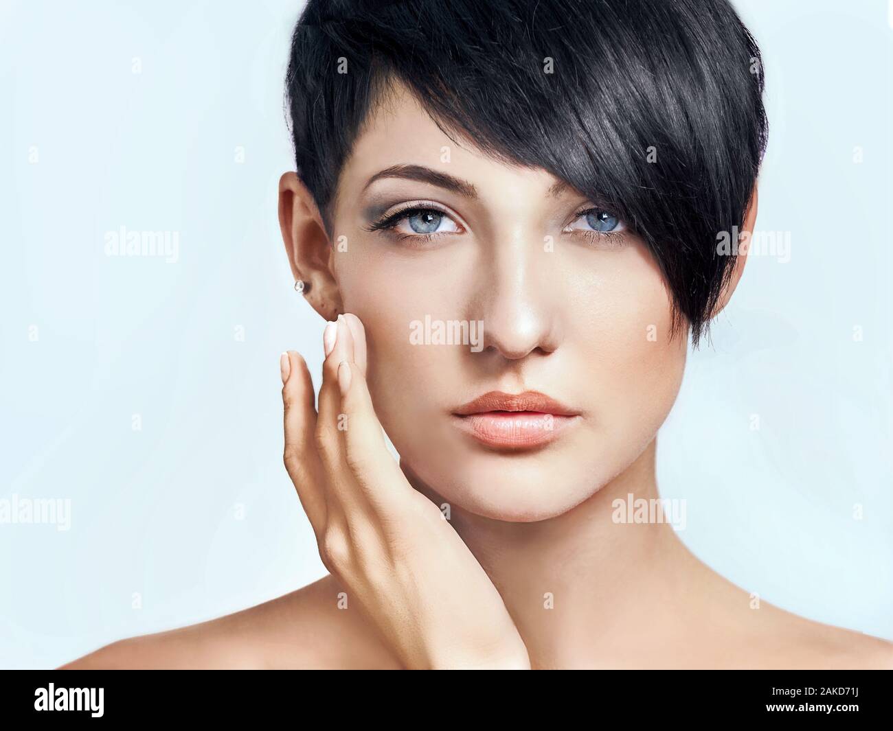 Close-up face of beautiful young brunette with short hairstyle. Hand touching her face. Skin care concept Stock Photo