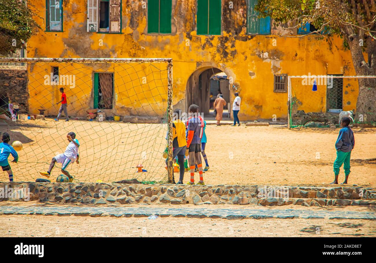 Goree island, Senegal- April 22 2019: Unidentified boys play soccer on the sand in the town in Africa. oys playing in front of an old yellow house on Stock Photo
