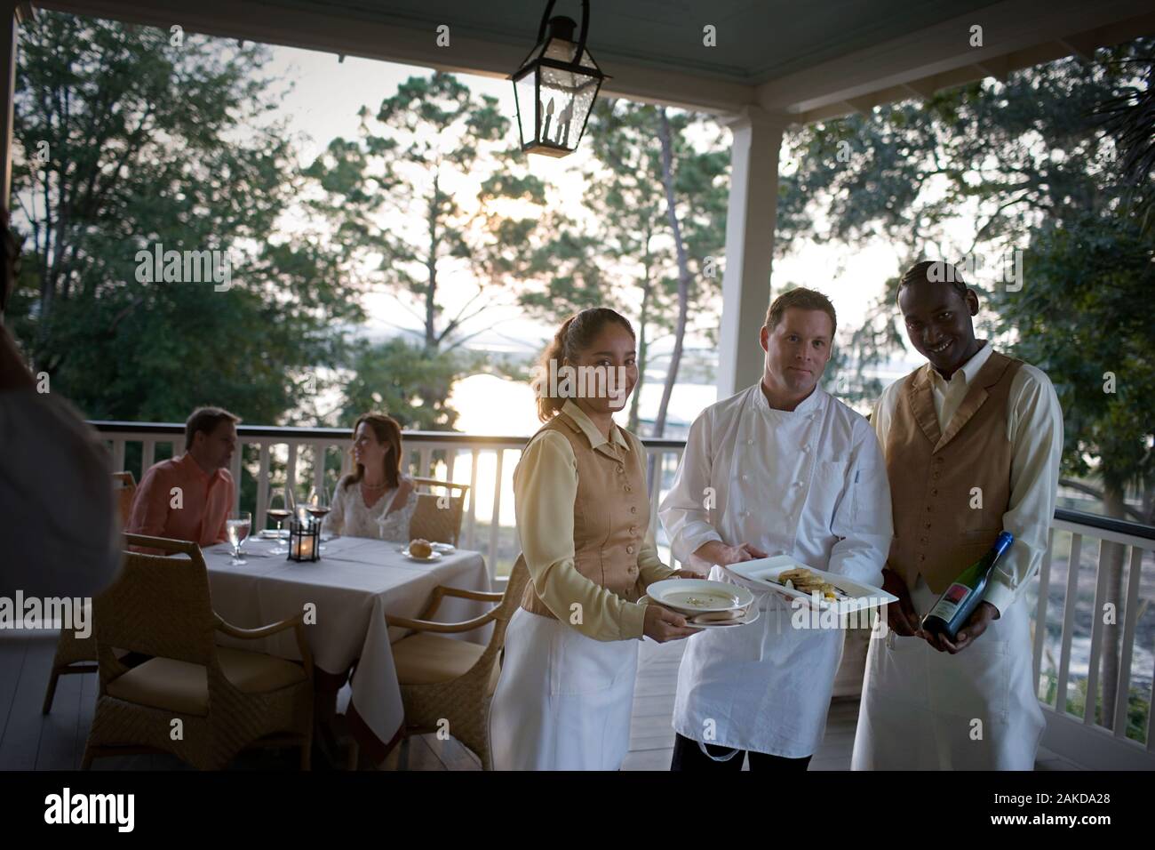 Portrait of a mid-adult male chef holding food with young adult male and female wait staff. Stock Photo