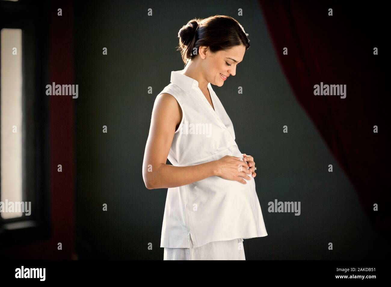 Pregnant young woman standing with her hand on her belly. Stock Photo