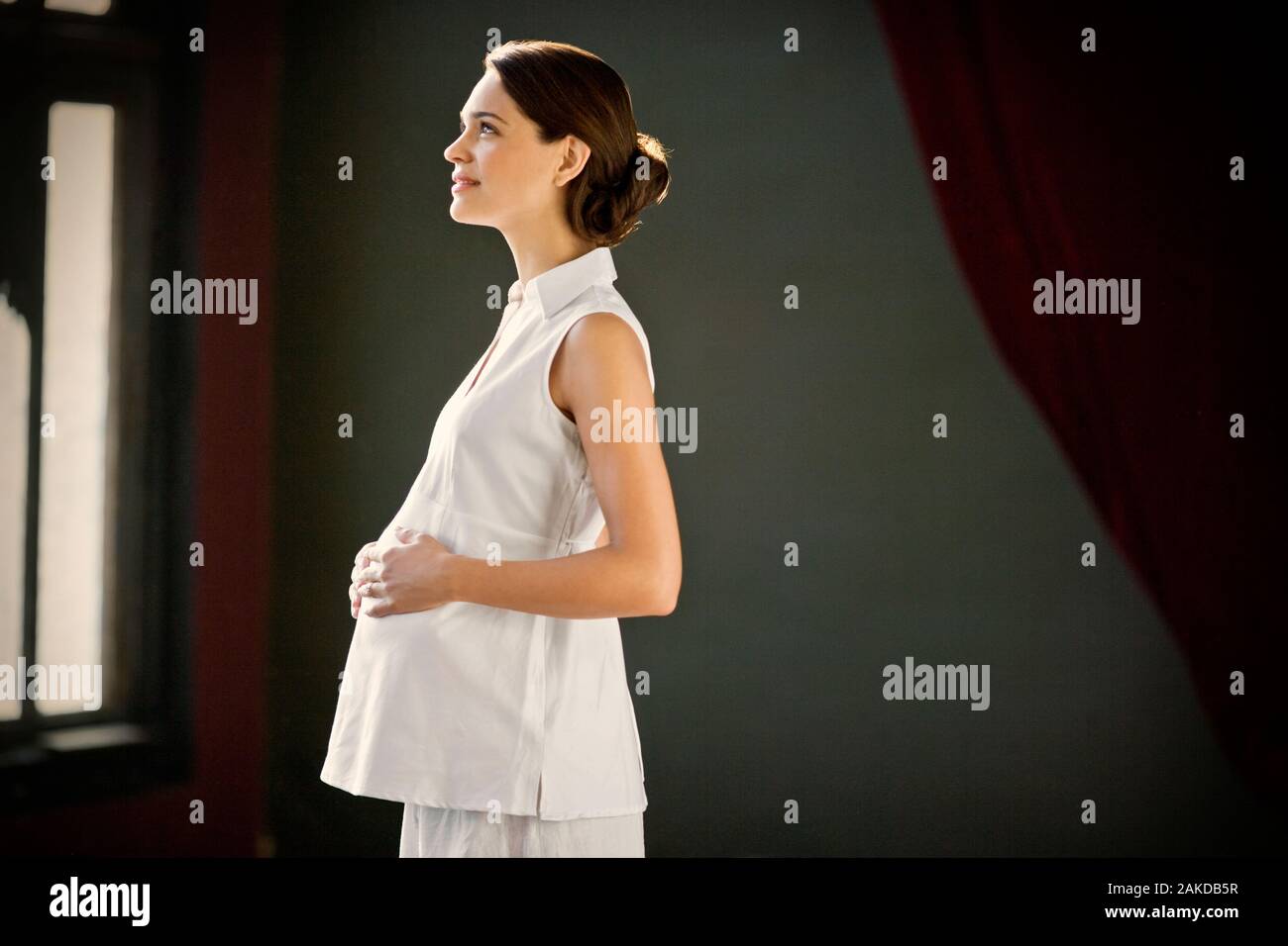 Pregnant young woman standing with her hand on her belly. Stock Photo