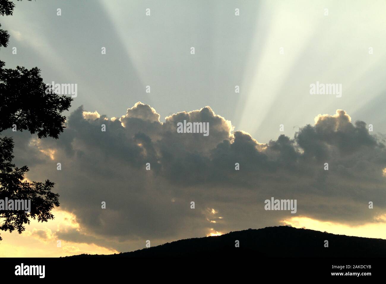 Sun rays emerging from behind a cloud before sunset Stock Photo
