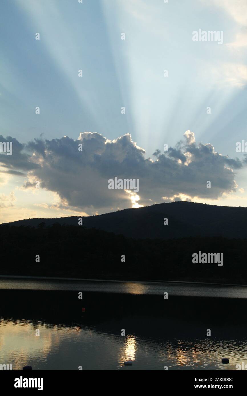 Sun rays emerging from behind a cloud before sunset Stock Photo