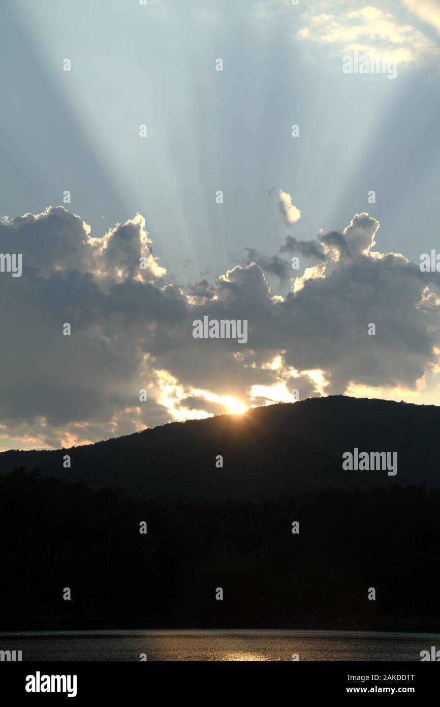 Sun rays emerging from behind a cloud before sunset Stock Photo