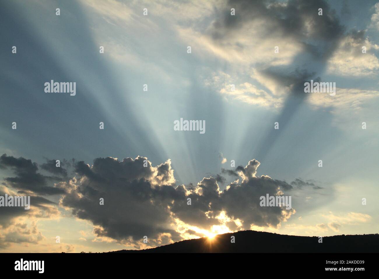 Sun rays emerging from behind a cloud before sunset Stock Photo