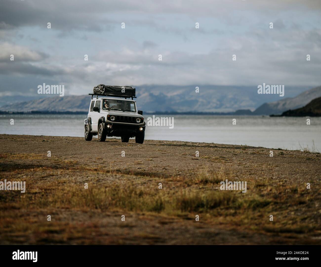 White SUV with tent  drives on a beach next to Lake Hawea, New Zealand Stock Photo