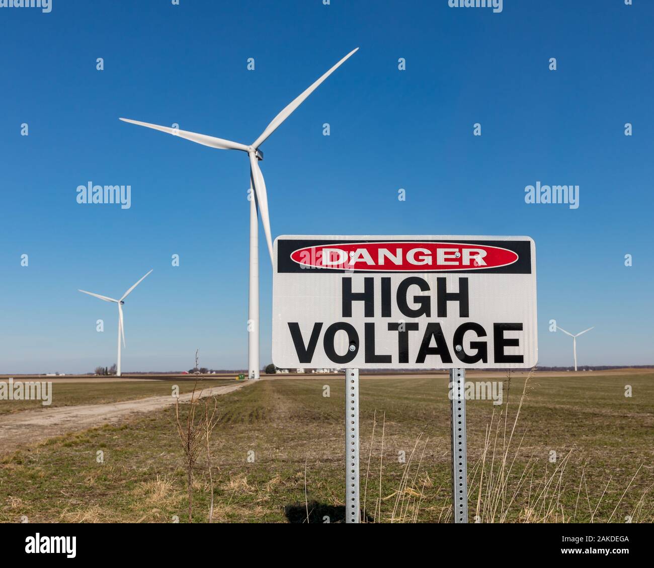 High voltage danger warning sign with wind turbine, windmill, in background. Concept of clean, green energy and danger of electricity Stock Photo