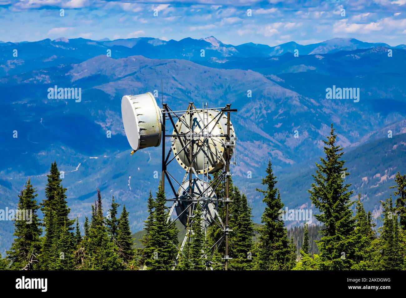 Juxtaposition of a cellular network tower emitting EMF radiation pollution in rural Canada with a scenic view of the Rocky Mountains and pine trees Stock Photo
