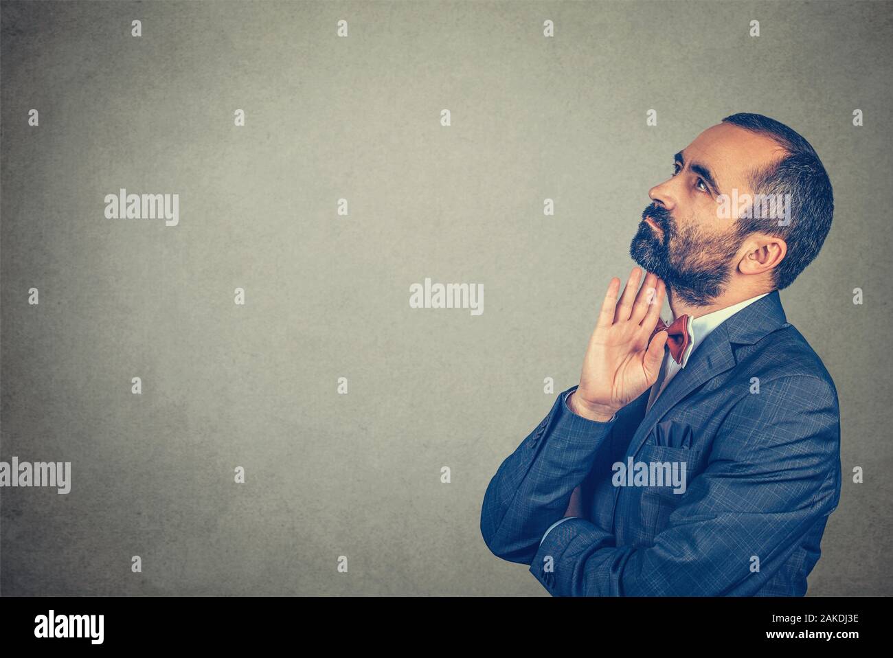 Thoughtful bearded businessman, wearing elegant jacket with red bow tie, standing with crossed arms, hand on chin and looking sidewards isolated gray Stock Photo