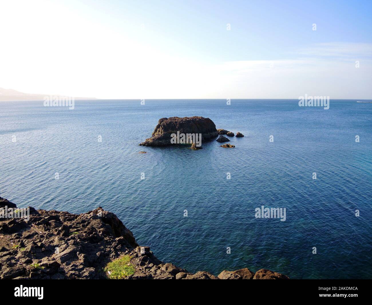 A rocky island on calm blue ocean surface. Stock Photo