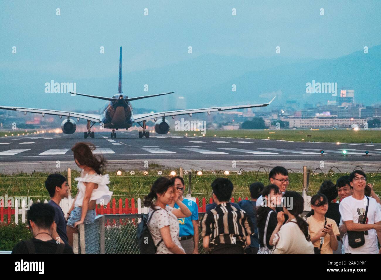Locals stand and watch a plane take off at 'Airplane Alley' in Taipei, Taiwan Stock Photo