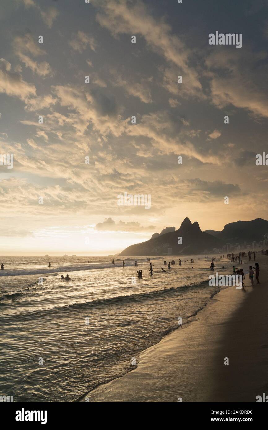A dramatic sunset over Ipanema Beach in Rio de Janeiro, with golden light shining on grey clouds. Stock Photo