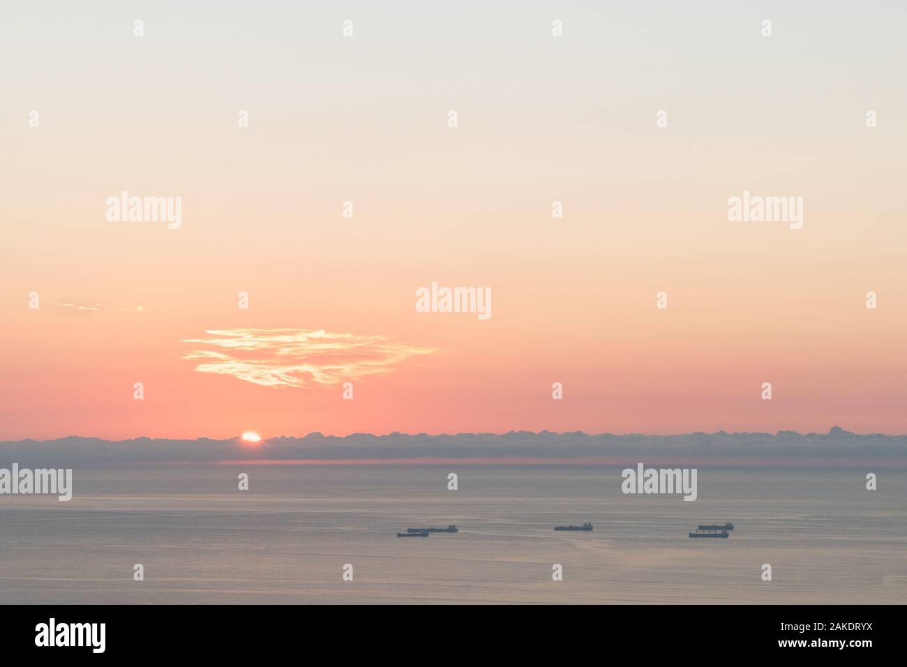 Minimalist shot of the sun peaking over the horizon over the water. The sky is a blue pink gradient. Stock Photo
